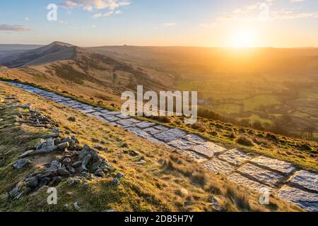 Steinwanderweg, der entlang des Grats des Mam Tor im British Peak District verläuft und die Sonne über dem Horizont aufgeht. Stockfoto