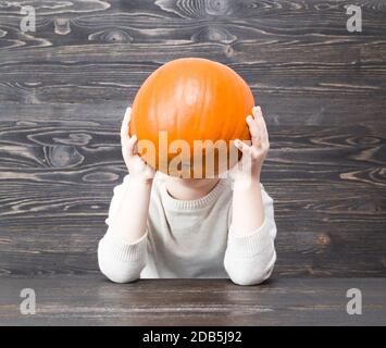 Orange Kürbis in den Händen eines Jungen auf dem Hintergrund eines schwarzen Holzbrett, Nahaufnahme Stockfoto