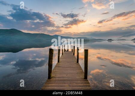 Lange hölzerne Anlegestelle mit Stöcken, die zum See bei Sonnenuntergang im Lake District, Großbritannien, führen. Stockfoto