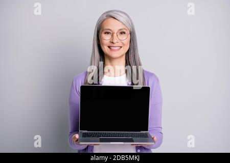 Foto-Porträt von lächelnd fröhlich glückliche Geschäftsfrau tragen Brillen halten Geöffneter Laptop in beiden Händen isoliert auf grauem Hintergrund Stockfoto