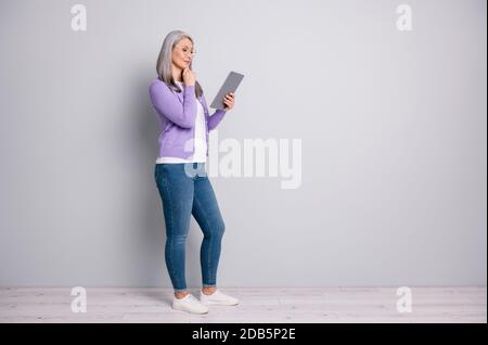 In voller Länge Körpergröße Foto von älteren Frau lächelnd arbeiten Mit Laptop lesen berühren ihr Gesicht tragen Brillen Casual Outfit Isoliert auf Grau Stockfoto