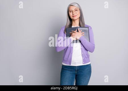 Das Lieblingsgedicht meiner Oma. Foto-Porträt von älteren weiblichen Literatur Liebhaber hält umarmt Buch trägt violette Strickjacke Jeans isoliert auf grau Stockfoto
