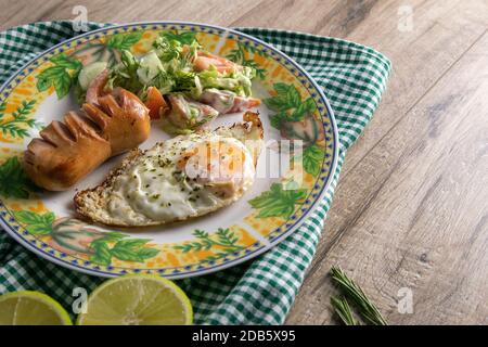 Englisches Frühstück, Rührei mit Wurst und Kohlsalat, daneben eine in zwei Hälften geschnittene Limette, ein Teller steht auf einem Holztisch. Stockfoto