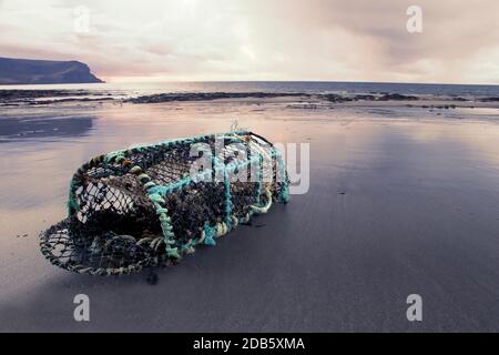 Verlassene offenen Kreelkäfig auf sandigen schottischen Strand mit Hügeln Im Hintergrund erhellt durch Sonnenuntergang Stockfoto