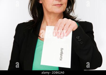 Cropped Oberkörperansicht einer Frau mittleren Alters in einem schwarzen Blazer mit ihrer linken Hand hält einen weißen Umschlag in Richtung der Kamera mit der Aufschrift ' Stockfoto