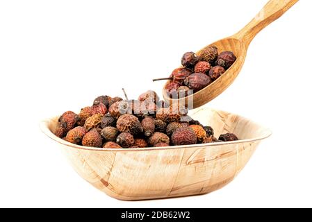 Trockene Hagebutten in einer Holzschüssel und Holzlöffel auf weißem Hintergrund. Stockfoto