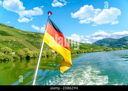 Deutsche Flagge auf einem Schiff mit Fluss mosel und Weinberg im Hintergrund Stockfoto