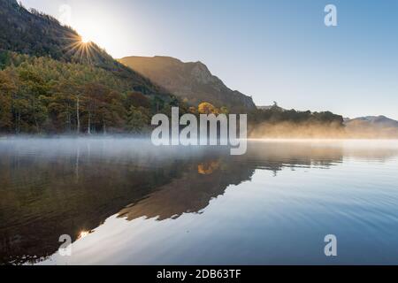 Ruhiger und friedlicher nebliger Herbstmorgen in Derwentwater im Lake District, wenn die Sonne über den Bergen aufgeht. Stockfoto