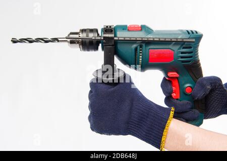 Männliche Hände halten einen elektrischen Bohrer. Hände in blauen Handschuhen. Bohren Sie auf einem weißen Hintergrund. Stockfoto