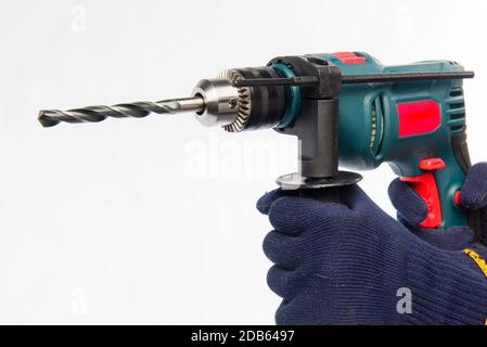 Männliche Hände halten einen elektrischen Bohrer. Hände in blauen Handschuhen. Bohren Sie auf einem weißen Hintergrund. Stockfoto