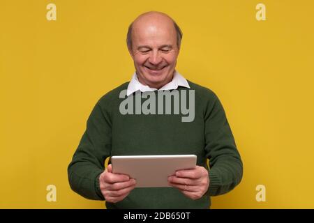 Elegante Senior Glatze Mann lächelt zuversichtlich bei der Kamera hält ein Tablet Stockfoto