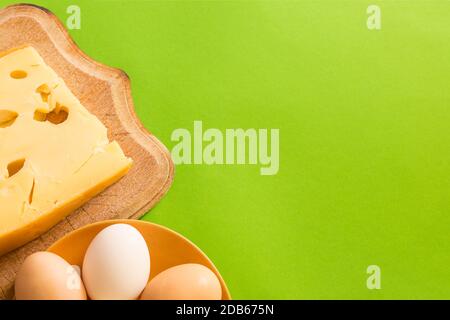 Maasdam Käse auf einem Brett mit Eiern auf einem Teller, auf einem grünen Hintergrund mit Kopierraum. Stockfoto