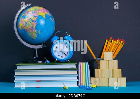 Die Kugel und die Uhr stehen auf einem Stapel Bücher, neben einem Glas Bleistifte und die Pyramide ist mit Holzwürfeln gefaltet. Stockfoto