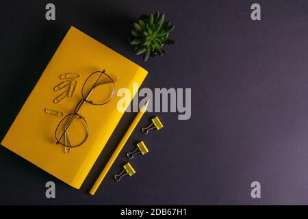 Gelber Bleistift, gelbes Notizbuch und Brille, Stifte, Clip-Papier auf schwarzem Hintergrund. Stockfoto