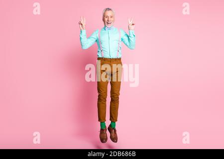 In voller Länge Körpergröße Seitenprofil Foto von glücklichen alten Mann springt mit Geste V-Zeichen mit beiden Händen isoliert auf Rosa Hintergrund Stockfoto