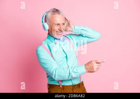 Portrait Foto von alten Gentleman Musik hören mit Wireless Kopfhörer zeigen mit Finger isoliert auf rosa Hintergrund Stockfoto