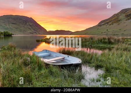 Wunderschöner, glühender Sonnenuntergang an einem ruhigen Frühlingsabend mit einem Ruderboot am Crummock Water im Lake District. Stockfoto