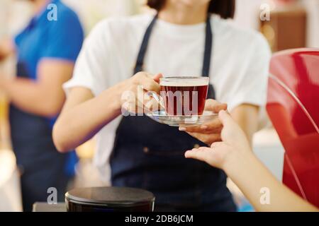 Kellnerin gibt dem Gast Kaffee Stockfoto