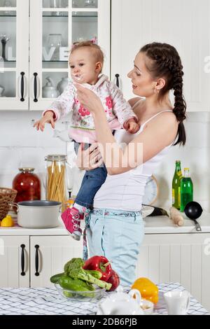 Junge Mutter füttert kleine Tochter in der heimischen Küche. Frohe Familie. Stockfoto