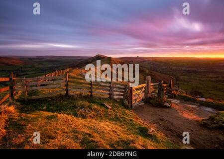 Glühendes rotes Licht von der aufgehenden Sonne, das auf dem Landschaftstor am Mam Tor im Peak District mit launischen Wolken scheint. Stockfoto