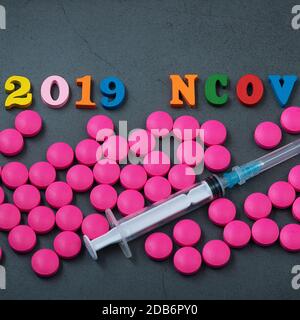Der Name der chinesischen Grippe, ihre Abkürzung. Rosa Pillen und eine Spritze sind auf einem grauen Hintergrund verstreut. Das Konzept der Behandlung von Influenza. Sal Stockfoto