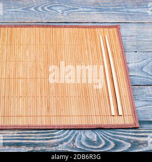 Zwei hölzerne Essstäbchen liegen auf dem Rand einer Bambusmatte, die auf einem Holztisch aus strukturierten Brettern sitzt. Stockfoto
