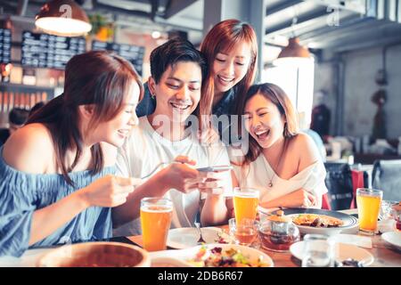 Fröhliche junge Leute sitzen im Restaurant und machen Fotos für Lebensmittel Stockfoto