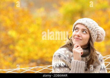 Nachdenkliche Frau sieht im Herbst auf einer Hängematte zur Seite In einem Wald Stockfoto