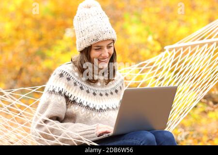 Glückliche Frau mit Laptop sitzen auf Hängematte in der Herbstsaison In einem Wald Stockfoto