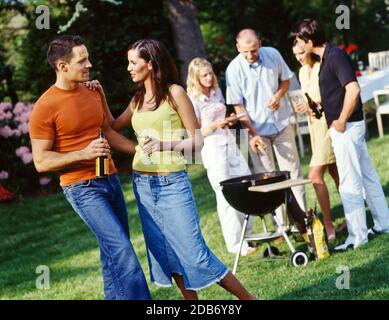 Freundliche junge Leute, die essen und trinken, kommen zusammen und haben Spaß im Garten mit Grillparty Stockfoto