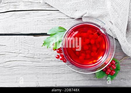 Tee mit Viburnum in einer Glasschale, Beeren und grüne Blätter, Burlap Serviette auf Holzbrett Hintergrund von oben Stockfoto