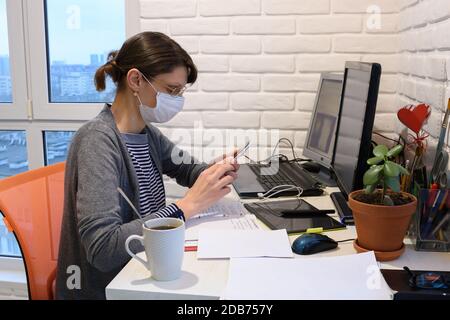 Ein krankes Mädchen in einer medizinischen Maske zu Hause kommuniziert am Telefon Stockfoto
