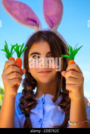 Portrait eines niedlichen Pre-Teen-Mädchens, das einen glücklichen christlichen Urlaub feiert, gekleidet als ein Osterbrötchen, das Karotten hält, im Garten im Hof Stockfoto