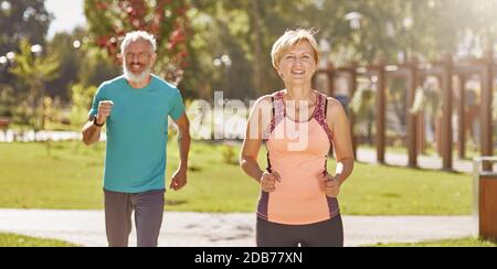 Für eine bessere Gesundheit. Aktives reifes Familienpaar in Sportswear, das beim gemeinsamen Laufen im Park an einem warmen sonnigen Tag glücklich aussieht. Freudiger Senior Stockfoto