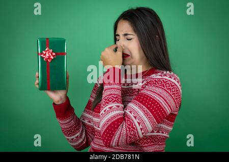 Junge schöne Mädchen halten Geschenk über isolierten weißen Hintergrund riecht etwas stinkend und ekelhaft, unerträglichen Geruch, Atem mit fing halten Stockfoto