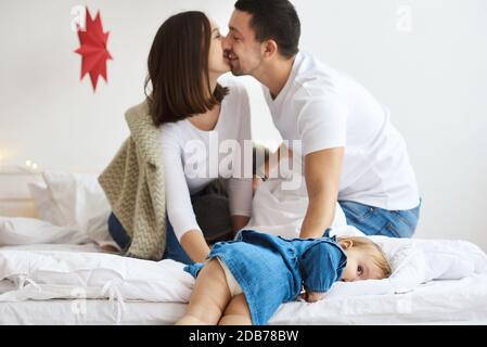 Glückliche Mutter Vater und Tochter spielen auf dem Bett im Schlafzimmer am Weihnachtsmorgen. Stockfoto