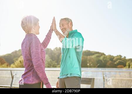 Partnerschaft. Glückliches Familienpaar, reifer Mann und Frau in Sportkleidung geben High Five nach dem Training im Stadtpark an einem sonnigen Morgen Stockfoto