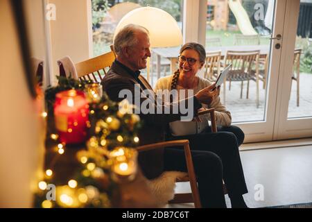 Ältere Männer und Frauen mit einem digitalen Tablet und lächeln während eines Videoanrufs. Seniorenpaar mit Tablet-Computer an einem Heiligabend zu Hause. Stockfoto