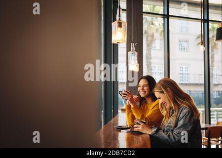 Zwei Freundinnen, die lachen und Spaß in einem Café haben. Zwei Frauen plaudern während sie Kaffee in einem Café trinken. Stockfoto