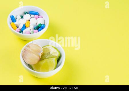 Limette und Ingwer gegen mehrfarbige Tabletten. Das Konzept der Wahl einer gesunden Ernährung gegenüber der Einnahme von Medikamenten. Von oben mit viel Platz. Stockfoto