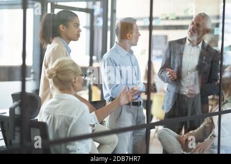 Multirassische Kollegen, die im Sitzungssaal eine Besprechung abhalten, über Geschäfte diskutieren und frische Ideen austauschen, während sie im modernen Büro zusammenarbeiten Stockfoto