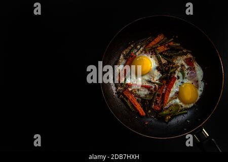 Zwei Spiegeleier in einer Pfanne mit großen Karotten-Scheiben, Paprika und Spargel mit Gewürzen und Sauce. Stockfoto