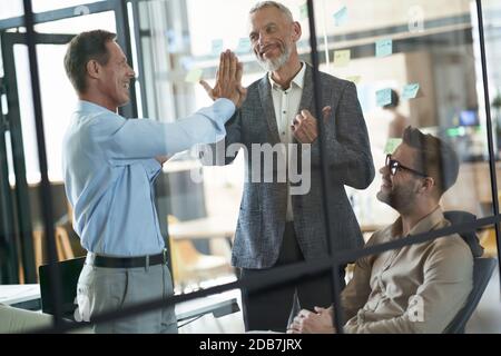Gut gemacht. Zwei glückliche reife Geschäftsleute geben sich hohe fünf, während ein Treffen mit Kollegen in der modernen Büro Stockfoto