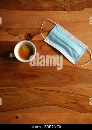 Kaffeetasse auf einem Holztisch neben einer Maske platziert. Draufsicht Stockfoto