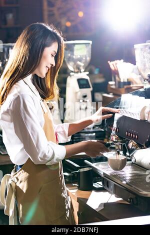 Seitenansicht eines Barista Brühkaffees von einer modernen Kaffeemaschine, um eine Tasse Kaffee mit einem anderen Barista zu machen, der im Hintergrund arbeitet. Verwenden für Stockfoto
