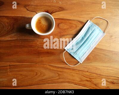 Kaffeetasse auf einem Holztisch neben einer Maske platziert. Draufsicht Stockfoto