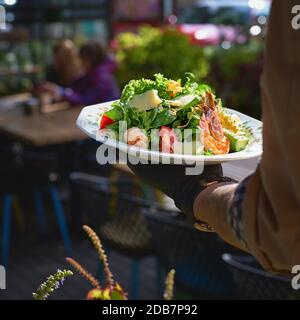 Frischer Sommersalat mit Garnelen in den Händen des Kellners auf der Terrasse. Gesunde Ernährung Konzept. Stockfoto