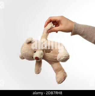 Weibliche Hand hält kleinen beige niedlichen Teddybären mit Flecken, Spielzeug auf weißem Hintergrund Stockfoto