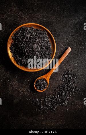 Flache Holzschüssel und Löffel mit schwarzen Salzkristallen Stockfoto