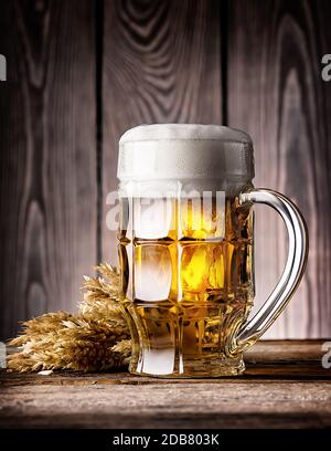 Facettierte Becher helles Bier mit Schaum und Ohren auf dem hölzernen Hintergrund Stockfoto